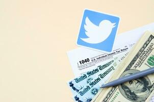 Twitter printed logo lies with 1040 Individual Income tax return form with Refund Check and hundred dollar bills on beige background. Help in tax period from social network concept photo