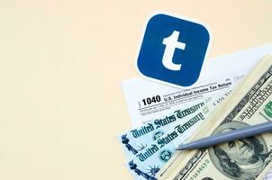 Tumblr printed logo lies with 1040 Individual Income tax return form with Refund Check and hundred dollar bills on beige background. Help in tax period from social network concept photo