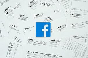 Printed Facebook logo on many tax form blanks lies on table close up. Help with tax problems using internet and information from social networks photo