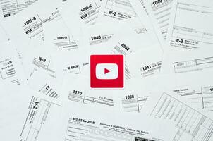 Printed Youtube logo on many tax form blanks lies on table close up. Help with tax problems using internet and information from social networks photo
