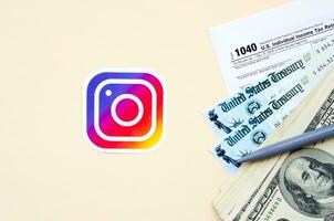 Instagram printed logo lies with 1040 Individual Income tax return form with Refund Check and hundred dollar bills on beige background. Help in tax period from social network concept photo