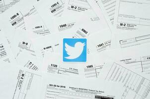 Printed Twitter logo on many tax form blanks lies on table close up. Help with tax problems using internet and information from social networks photo