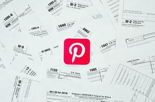 Printed Pinterest logo on many tax form blanks lies on table close up. Help with tax problems using internet and information from social networks photo