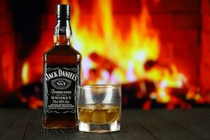 KYIV, UKRAINE - MAY 4, 2022 Jack Daniels original alcohol bottle on wooden table with red fireplace photo