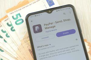 TERNOPIL, UKRAINE - AUGUST 3, 2023 PayPal application on screen on modern smartphone and many bills of euro currency photo