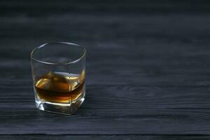 Glass with cognac or whisky alcohol drink on black wooden table close up with copy space for text. Elite alcohol drinking or alcoholism concept photo