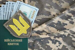 Symbol of Ukrainian army and military ID with bunch of money on the camouflage uniform of a Ukrainian soldier. Concept of payment to military personnel or bribe for deferment from service photo