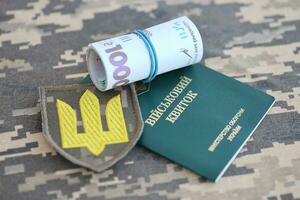 Symbol of Ukrainian army and military ID with bunch of money on the camouflage uniform of a Ukrainian soldier. Concept of payment to military personnel or bribe for deferment from service photo