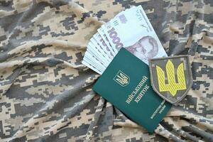Symbol of Ukrainian army and military ID with bunch of money on the camouflage uniform of a Ukrainian soldier. Concept of payment to military personnel or bribe for deferment from service photo