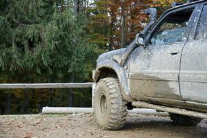 Wheel closeup in a countryside landscape with a mud road. Off-road 4x4 suv automobile with ditry body after drive in muddy road photo