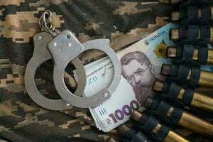 Ukrainian army machine gun belt shells and handcuffs on military uniform. Concept of bribery and war crimes photo