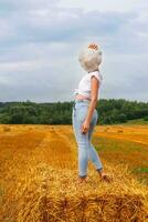 girl in straw hat stands on a haystack on a bale in the agricultural field after harvesting photo