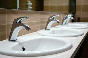 Modern public bathroom with row of white ceramic wash sink basins and faucet with mirror in restroom concept by AI Generated photo