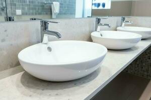 Modern public bathroom with row of white ceramic wash sink basins and faucet with mirror in restroom concept by AI Generated photo