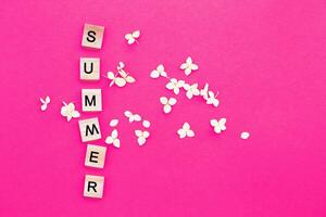 Word summer written from a wooden cube on pink background with a petals of a hydrangea flowers photo