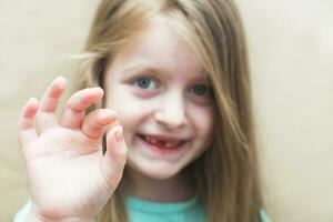 Little cute blonde girl child holding and showing her fallen milk front tooth in hands photo