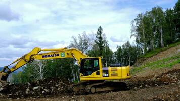 A yellow excavator works in the mountains. Construction of roads video