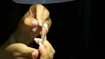 A manicurist applies gel nail polish to empty tips as a sample video