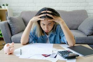 Asian female sitting expression face stressed by calculate expense on table from invoice or bill. She had financial and cost of living problems. photo