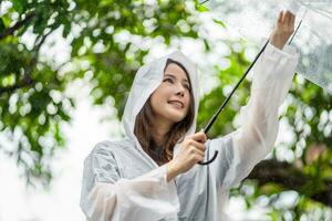 Young asian woman spreading umbrellas playing in the rain, she is wearing rainwear. photo