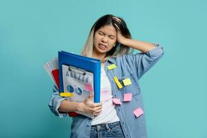 Upset office worker with a lot of work on hand trying to get everything done on time. She is holding a folder of documents standing isolated on bright blue background. photo