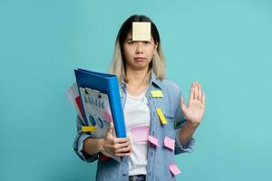 Serious Asian female office worker stops making gestures and puts his hand in front of the camera to stop something. She prepares for graph report with notepad isolated on blue studio background. photo