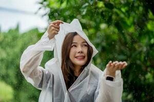 contento asiático mujer vistiendo un impermeable ella disfruta el lluvia en el parque. foto