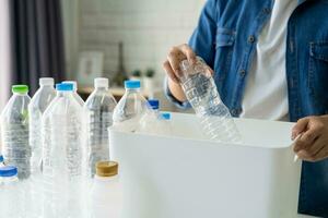 Woman hand holding recycle plastic bottle put in paper garbage bin at home photo