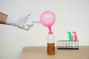 Hand points  to pink inflated balloons on top of transparent test bottles.Mix soft drink with baking soda powder  in bottle. Concept, science experiment about reaction of chemical substance. photo