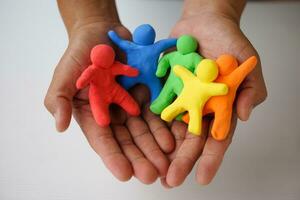 Close up hands holds colorful plasticine people. Human figures from plasticine sculpture.  Concept, friendships, partnerships and relationships between people. Sculting enhance imagination. photo