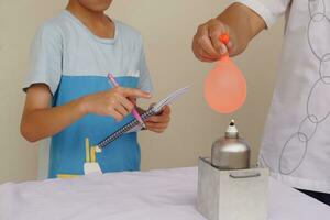 estudiante estudiar a hacer Ciencias experimentar acerca de reacción de aire en globo con agua lleno es quemado en fuego fuego de metal linterna. concepto, Ciencias lección, actividad a escuela. foto