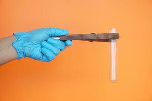 Close up hands wears blue glove, hold wooden tong to hold transparent test tube. Concept, science tool for doing experiment. Education. Science subject. Learning by doing. photo