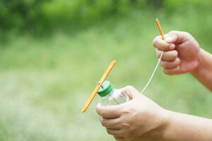 Close up hands hold DIY toy made from plastic bottle, rope and ice cream stick. Concept, Recycle crafts. Toy for kids, Teaching aid, fun activity for active learning. Spin for movement. DIY helicopter photo