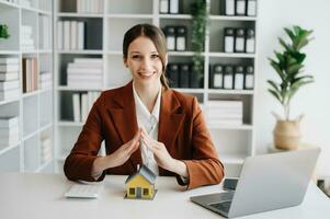 Female real estate agent is use hands to protect red roof for the concept of real estate investment about house trading, purchase at desk in office photo