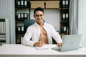 joven hermoso hombre trabajando a oficina con computadora portátil, tableta y tomando notas en el papel. foto