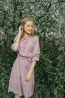 rubia niña en un primavera caminar en el jardín con Cereza flores hembra retrato, de cerca. un niña en un rosado polca punto vestido. foto