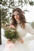 Beautiful bride in a white dress with a bouquet in a snow-covered winter forest. Portrait of the bride in nature. photo