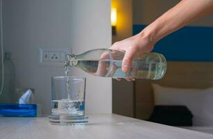 el mano de un blanco hombre torrencial un vaso de agua en el mesa. dentro el habitación a cura sed y salud cuidado por Bebiendo un lote de agua foto