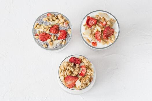Tres lentes de durante la noche chia semilla pudín con almendra leche, yogur, hecho en casa Granola, seco fresas, Almendras. superalimento y vegano comida concepto. Copiar espacio, selectivo enfocar, blanco antecedentes foto
