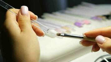 A manicurist applies gel nail polish to empty tips as a sample video