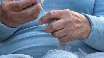 une femme avec tricot dans sa mains. le mains de un vieux femme à travaux d'aiguille. une femme dans bleu dissout une de laine foulard. tricot concept, retraité tranquille insouciant la vie . video