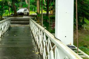 painted white iron fence Brown rust was growing on the wooden bridge. In front of the bridge was a white car parked and blur. photo