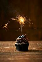Birthday chocolate cupcake with a sparkler on a rustic old table with brown colour background. Monochromatic colour pallet. Celebration. Copy space. photo