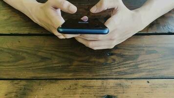 Video footage, top view of man's hand using smartphone on wooden table. Reply to messages with smartphone.