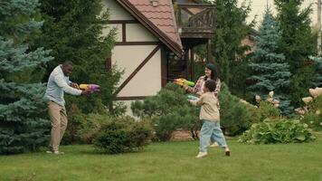 Cheerful family shoot at each other with water guns near the house on the lawn. video