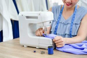 happy young asian female sitting with sewing machine,working, smiling experienced tailor is sewing clothes at factory,concept of sewing,worker,working,craft,tailoring,dressmaking,business,industry photo