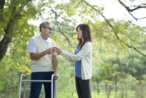 a daughter serving a drink to her father while go for walk and picnic in the park,a disability senior man use walker rehability by practice walking.concept holidays,elderly rehab,family relationship photo