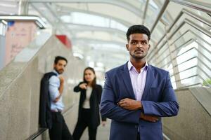 young executive standing with arms crossed is suspiciously, background are employee talking about him as bullying. concept advertising,article,magazine etc for management conflict in the workplace etc photo