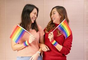 young asian lesbian marriage couple smile,look each other eye,holding lgbt rainbow gay pride flags,support of lgbtq community as transsexual, homosexual,transgender,movement,parade,celebrate photo