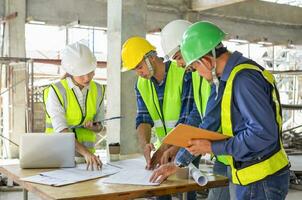 engineering teamwork wearing full safety gear discussing with blueprint and laptop on table in a new building under construction,engineers project manager consultation meeting with coworker photo